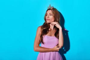 Problems in the kingdom. Thoughtful young woman in tiara looking away while standing against blue background photo