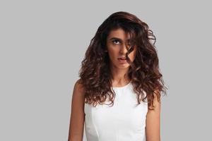 Her hair gives her trouble. Attractive young woman looking away while standing against grey background photo