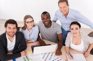 Strong business team. Top view of group of business people in casual wear sitting together at the table and smiling at camera photo