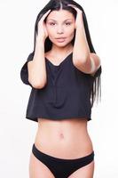 Sweet seduction. Attractive young woman in black underwear holding hands in hair and looking at camera while standing against background photo