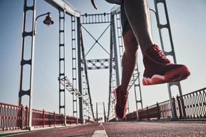 On the move. Close up of young man in sports clothing exercising while jogging on the bridge outdoors photo