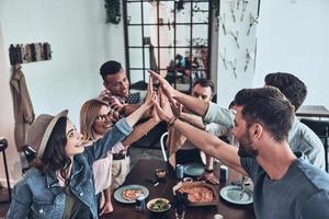 Happy together Top view of young people giving each other high-five in a symbol of unity and smiling while having a dinner party photo