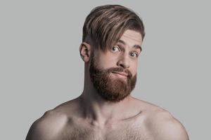 Portrait of young man looking at camera with surprised face while being in front of grey background photo