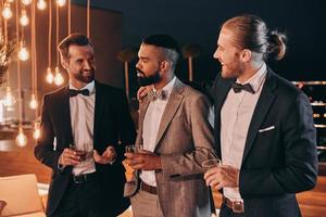 Three happy men in suits holding glasses with whiskey while spending time on party photo