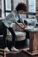 Young perfectionist. Beautiful young African woman using computer while leaning on the table photo