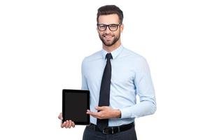 copie el espacio en su tableta. joven apuesto y seguro de sí mismo con camisa y corbata sosteniendo una tableta digital y apuntándola con una sonrisa mientras se enfrenta a fondo blanco foto