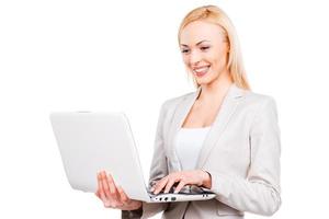 Confident businesswoman at work. Confident mature businesswoman working on laptop and smiling while standing against white background photo