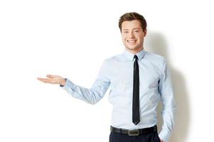 sosteniendo espacio de copia. Apuesto joven en camisa y corbata con espacio de copia y sonriendo mientras está de pie aislado en blanco foto