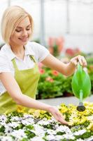 las flores necesitan mi cuidado. hermosa mujer de cabello rubio en uniforme regando flores foto