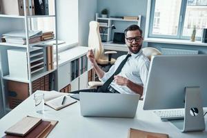 Happy young man in shirt and tie relaxing by listening music while sitting in the office photo