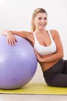 mujer en clase de pilates. hermosa mujer madura apoyada en la pelota de fitness mientras se sienta en la alfombra de ejercicio y sonríe foto