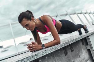 Never give up Modern young woman in sports clothing keeping plank position while exercising outdoors photo