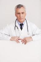 Doctor leaning at copy space. Senior grey hair doctor in uniform looking out of copy space and smiling while isolated on white photo
