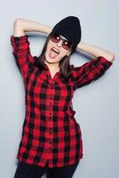 She is really cheeky. Attractive young woman in glasses posing and looking at camera while standing against grey background photo