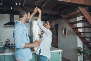 hermosa pareja joven sonriendo y bailando mientras pasa tiempo en la cocina foto