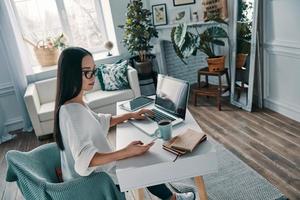 trabajando desde casa. vista superior de una hermosa joven que trabaja usando una laptop mientras está sentada en la oficina en casa foto