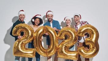 Group of young beautiful people in Christmas hats carrying gold colored numbers  and smiling photo