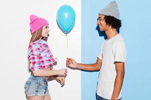 Add some colors. Handsome young African man giving a blue balloon to his girlfriend while standing against colorful background photo