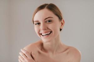 Pure beauty. Portrait of attractive young woman with freckles on face smiling and looking at camera while standing against grey background photo