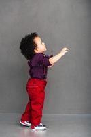 Lets go with me Side view of little African baby boy looking away and stretching out his hand while standing against grey background photo