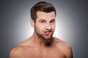 Playful mood. Portrait of handsome young shirtless man looking at camera and grimacing while standing against grey background photo