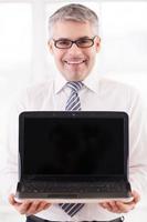 Your advertisement here. Smiling senior man in shirt and tie holding laptop and showing the monitor to you photo