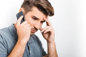 Bad news. Depressed young man talking on the mobile phone and touching face with hand while leaning at the wall photo