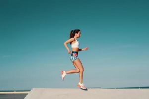 el deporte es el camino de su vida. toda la longitud de una hermosa joven con ropa deportiva trotando mientras hace ejercicio al aire libre foto
