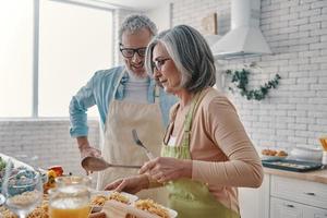 pareja mayor en delantales preparando una cena saludable y sonriendo mientras pasa tiempo en casa foto