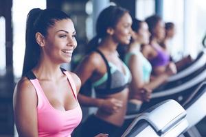 Jogging with smile. Side view close up of young beautiful women looking away with smile while running on treadmill at gym photo