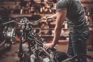 Man examining motorcycle. Close-up of young man examining motorcycle in repair shop photo