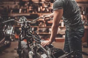 hombre examinando motocicleta. primer plano, de, joven, examinar, motocicleta, en, taller de reparación foto