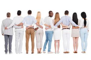 Happy to be in team. Full length rear view of group of diverse people bonding to each other and standing against white background while one African man looking over shoulder and smiling photo