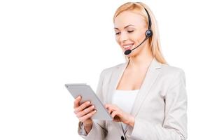 She knows how to help you. Confident mature customer service representative working on digital tablet and smiling while standing against white background photo
