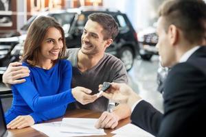 Now her dream comes true. Car salesman giving the key of the new car to the young attractive owners photo