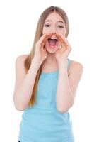 Announcing good news. Cheerful teenage girl shouting and holding hands near mouth while standing isolated on white photo