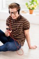 Relaxing with music. Top view of handsome young man looking at his mp3 player and listening to the music while sitting on the floor at his apartment photo