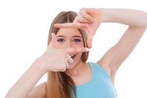 Focusing at you. Happy teenage girl focusing at you with finger frame and smiling while standing isolated on white photo