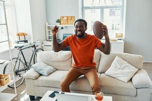 Happy young African man cheering and smiling while watching sport match at home photo