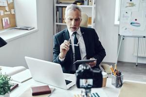 Senior man in elegant business suit using digital tablet while making social media video photo