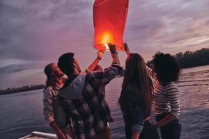 Having fun. Group of young people in casual wear holding sky lantern while standing on the pier photo