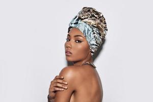 Calm and beautiful. Attractive young African woman in turban looking at camera while standing against grey background photo