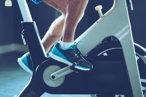 Intense cardio workout. Side view close-up part of young man in sports shoes cycling at gym photo