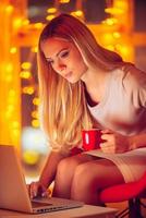 Busy even on holidays. Beautiful young woman in smart casual wear working on laptop with Christmas lights in the background photo