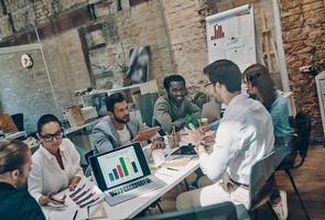 Group of young modern people in smart casual wear using modern technologies while working in the board room photo