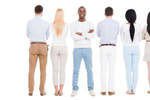 Everyone will get a chance. Rear view of group of people standing in a row and against white background while one cheerful African man standing face to camera and smiling photo