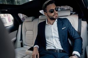 This is going to be a long day. Handsome young man in full suit looking away while sitting in the car photo