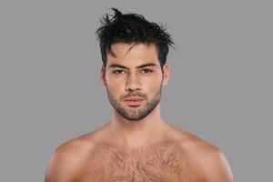 Young and handsome. Good looking young man looking at camera while standing against grey background photo