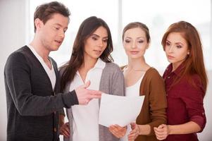 Discussing a contract. Group of young people discussing document while standing close to each other photo