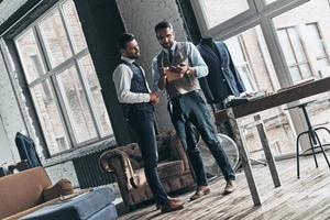 Taking notes. Full length of two young fashionable men having a discussion while standing in workshop photo